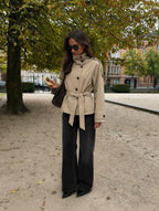 Woman wearing the Blair Belted Waist Cropped Trench Jacket in Khaki, styled with wide-leg black trousers and black heels, photographed outdoors in an autumn setting