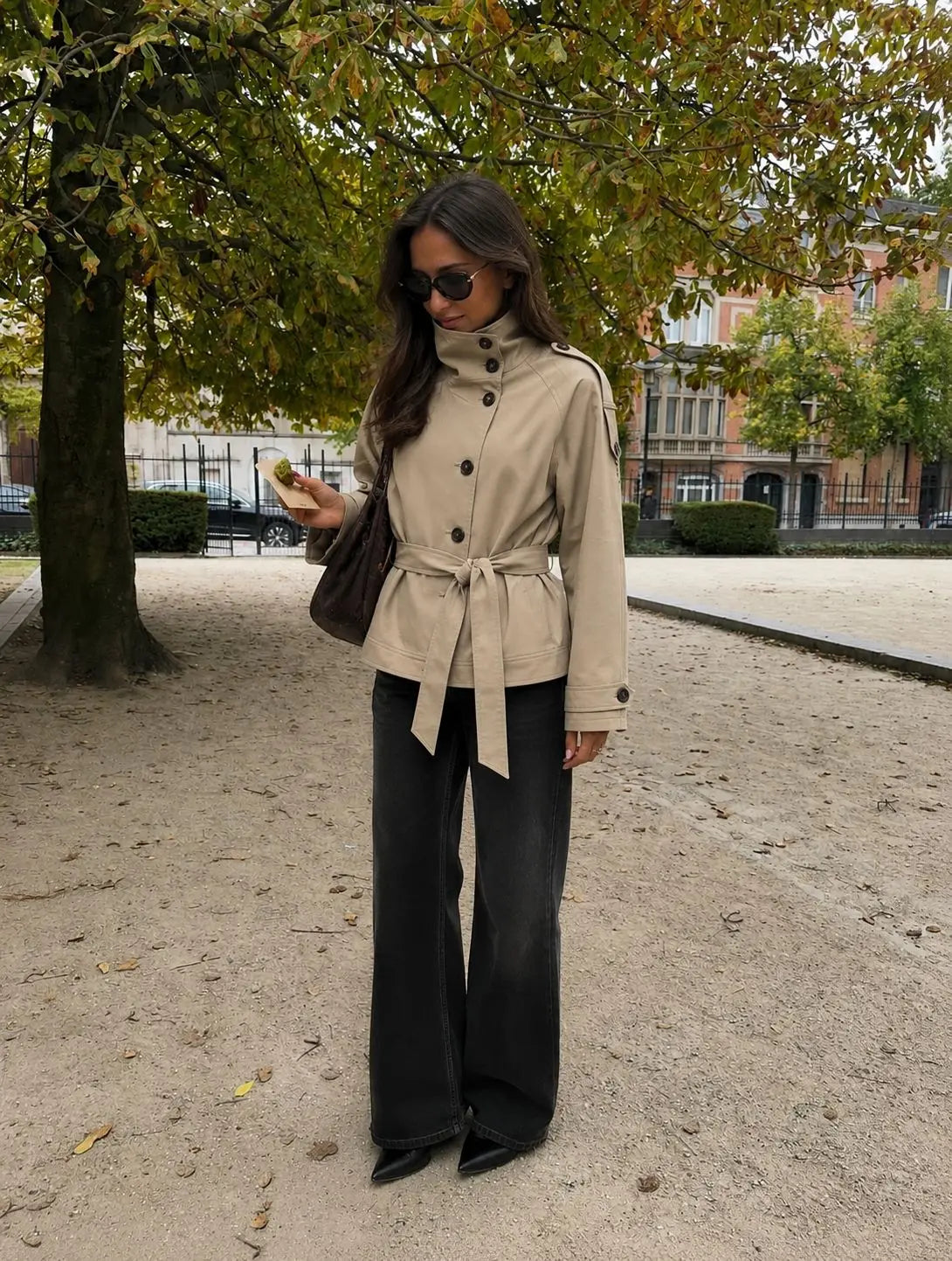 Woman wearing the Blair Belted Waist Cropped Trench Jacket in Khaki, styled with wide-leg black trousers and black heels, photographed outdoors in an autumn setting